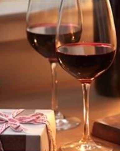 Zwei Gläser Rotwein, ein Geschenk und Pralinen bei Kerzenlicht
